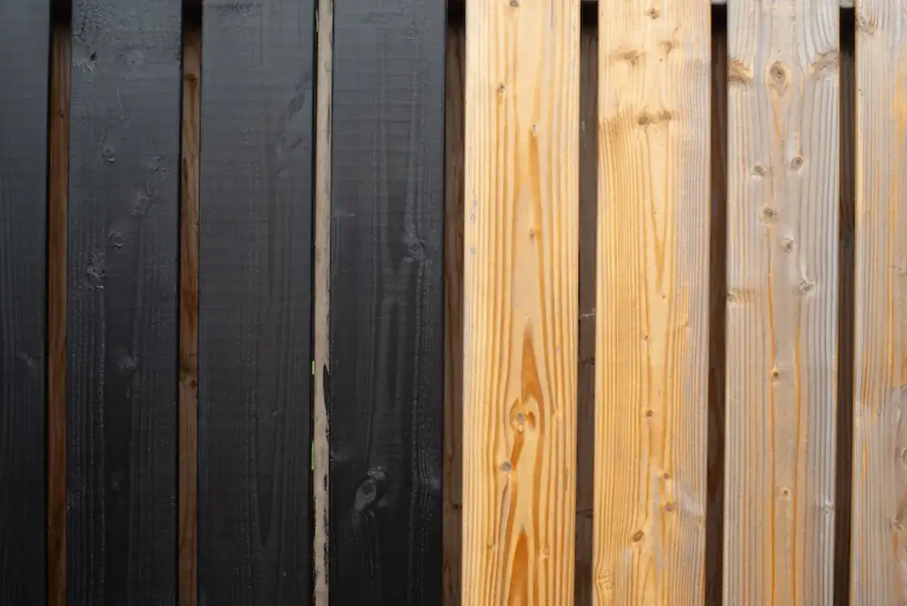 Holzlasur schützt Holz. Hier eine Seite schwarz lasiert, daneben unbehandeltes Holz.