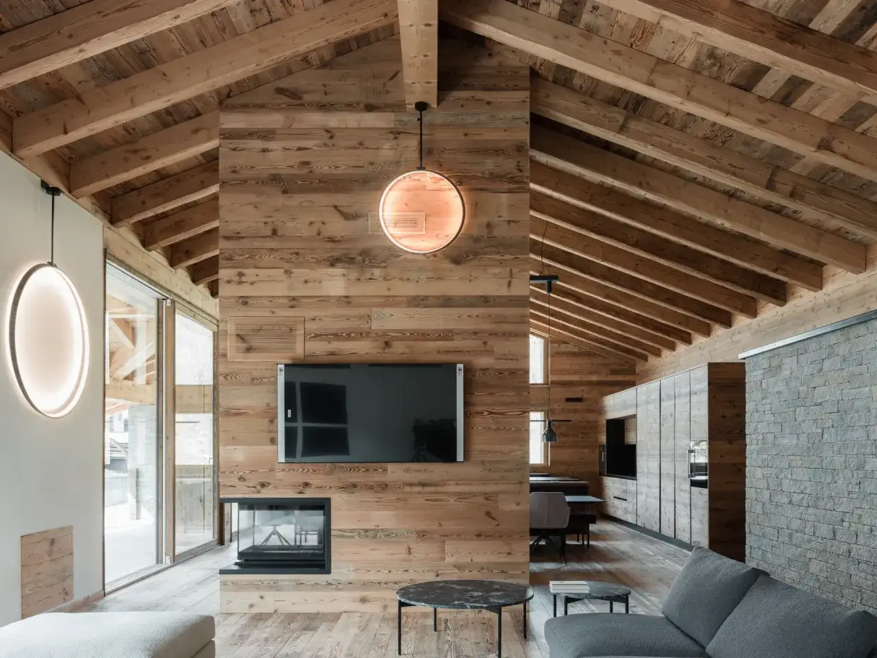 Gemütliche luxus chalet inneneinrichtung mit Holzwänden, Kamin, moderner Beleuchtung und Blick auf die Berge.