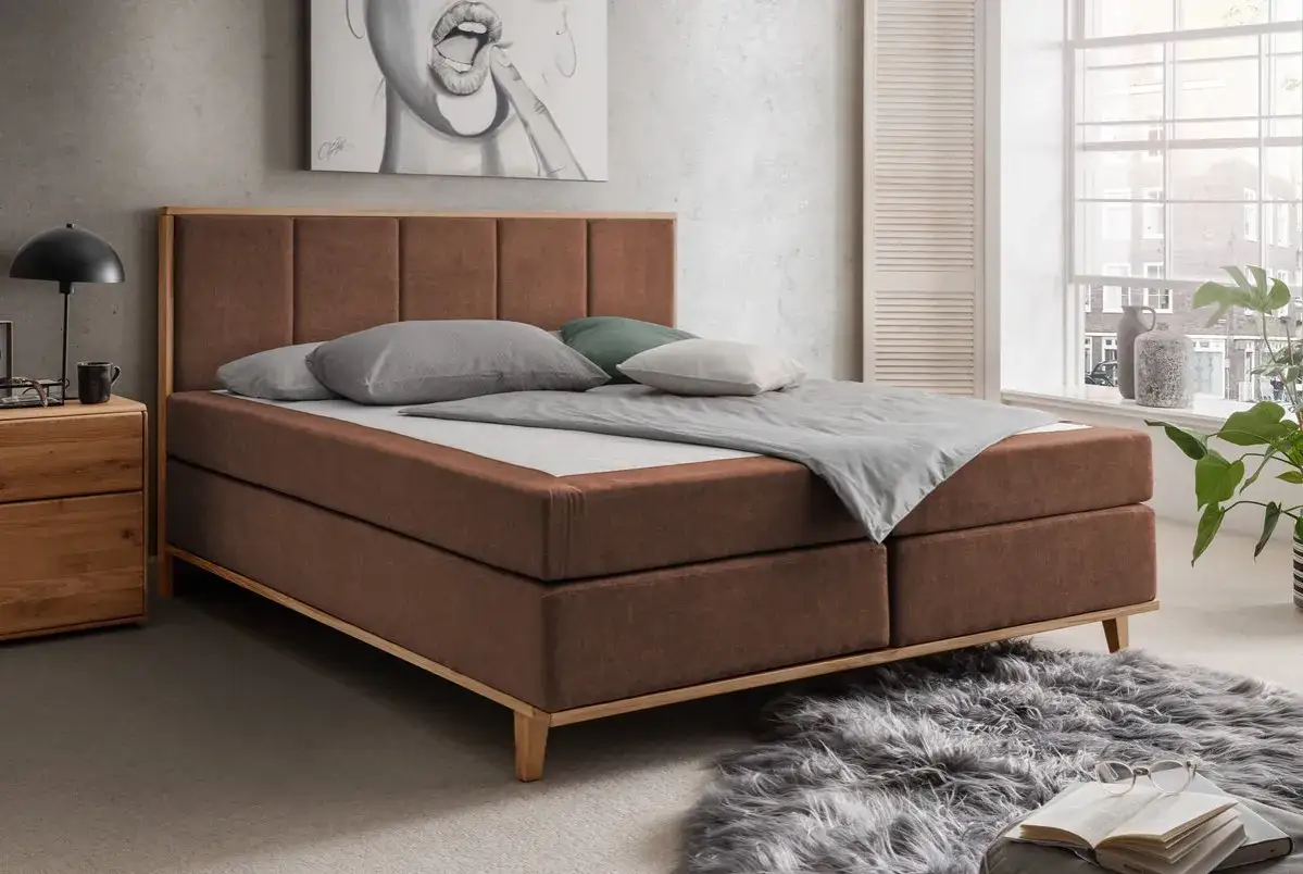 Gem&uuml;tliches Boxspringbett in Braun, ideal f&uuml;r Allergiker. Mit stilvollem Kopfteil und Holzakzenten.