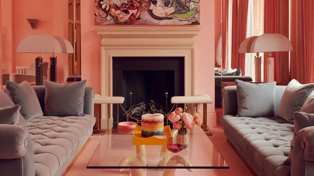 Ein luxuri&ouml;ses Wohnzimmer in zartem Rosa, das die Wirkung von Farben zeigt. Graue Sofas und ein Kamin schaffen Kontrast.