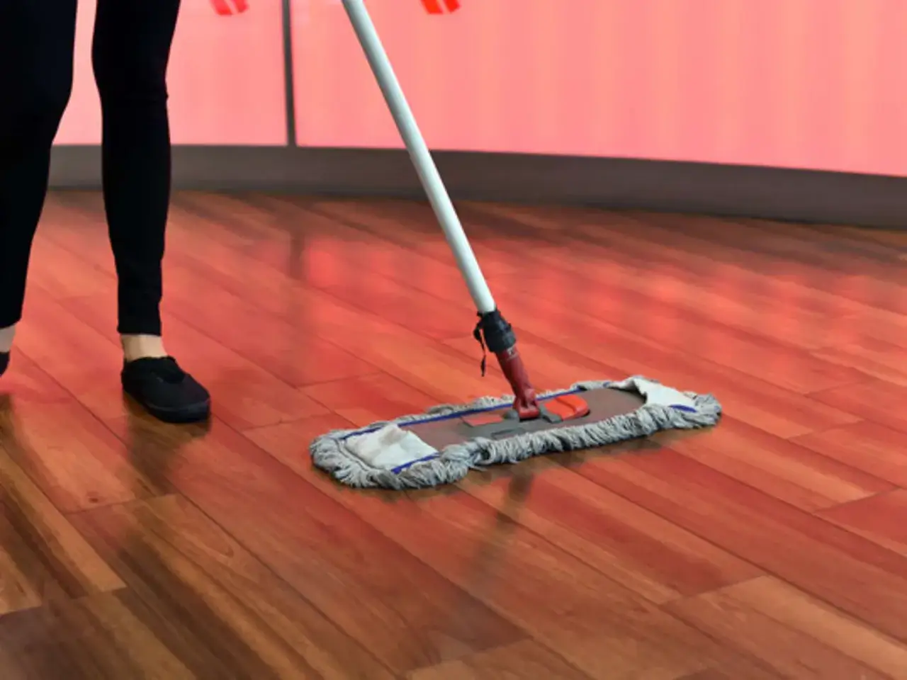 Person reinigt mit einem Mopp den gl&auml;nzenden Parkettboden.