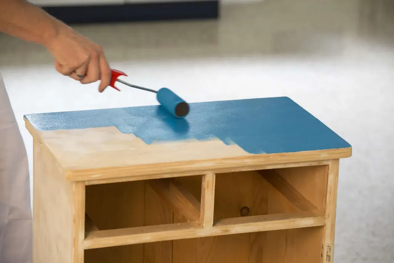 Hand rollt eine Kommode in leuchtendem Blau. Der Prozess, eine Kommode zu lackieren, verwandelt das Holzmöbelstück.