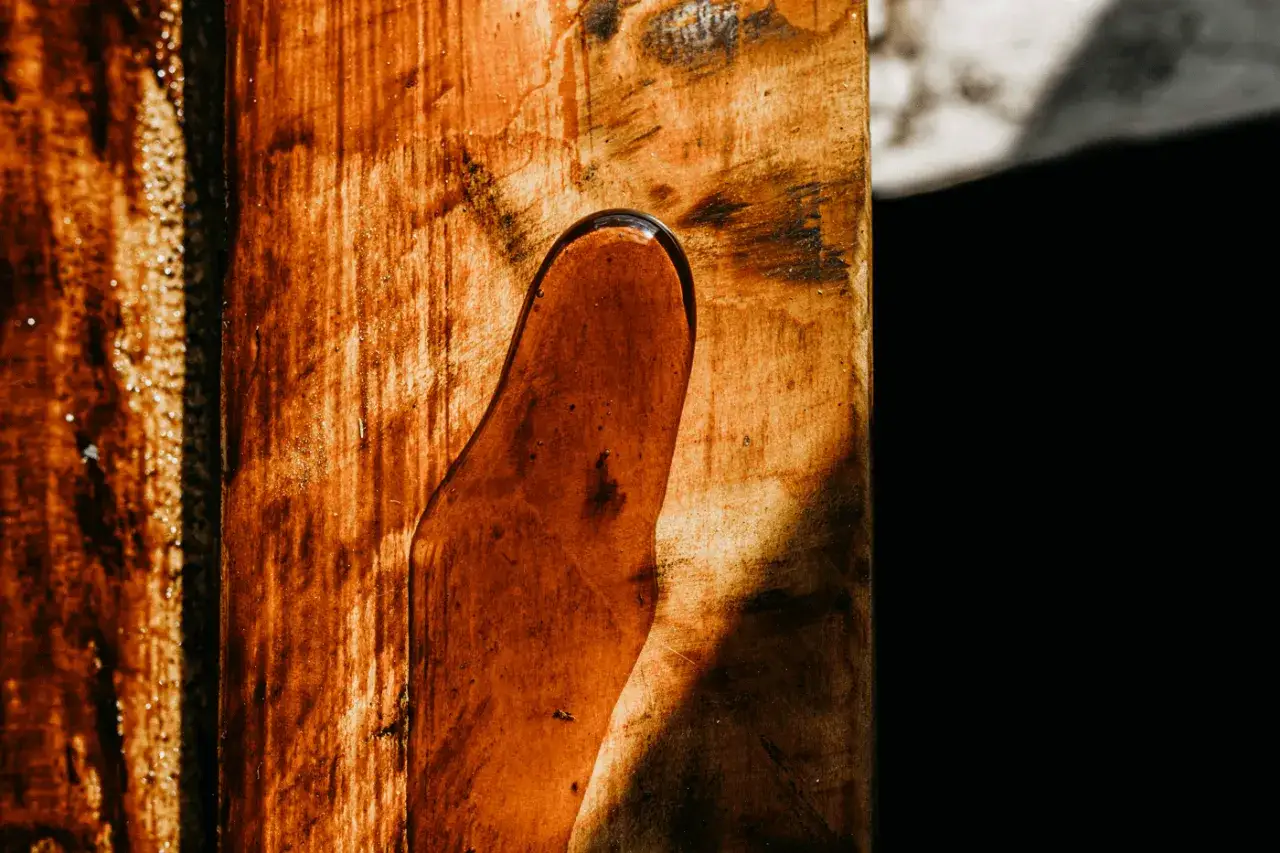 Flüssiges Harz tropft von einem Holzstück. Die braune, klebrige Masse glänzt im Licht. Ein Prozess, um Harz von Holz zu entfernen, ist hier sichtbar.