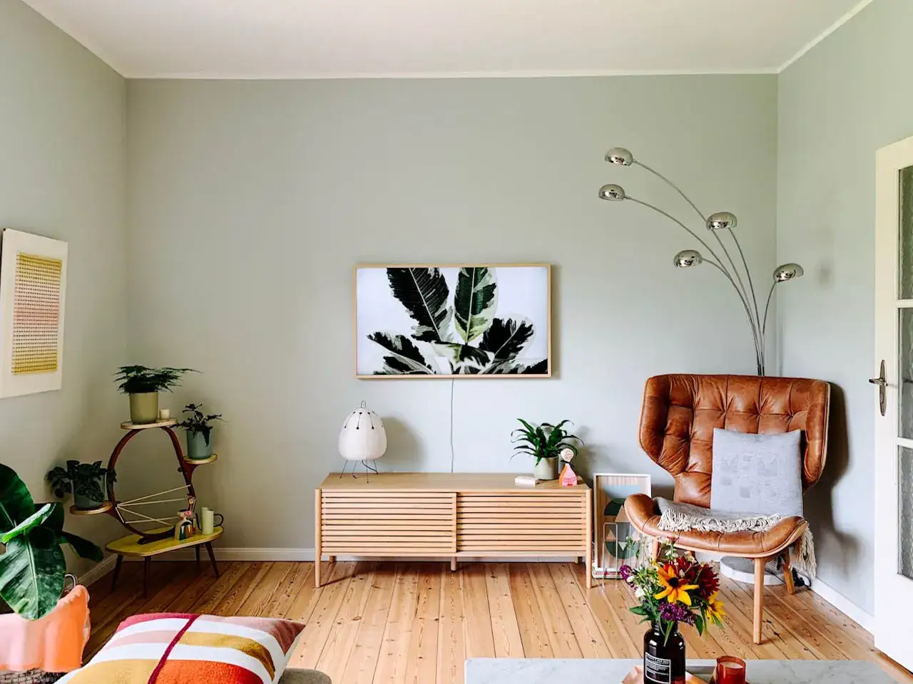 Helles Wohnzimmer mit sanften wandfarben, einem Ledersessel, Pflanzen und einem Bild mit Blattmotiv.