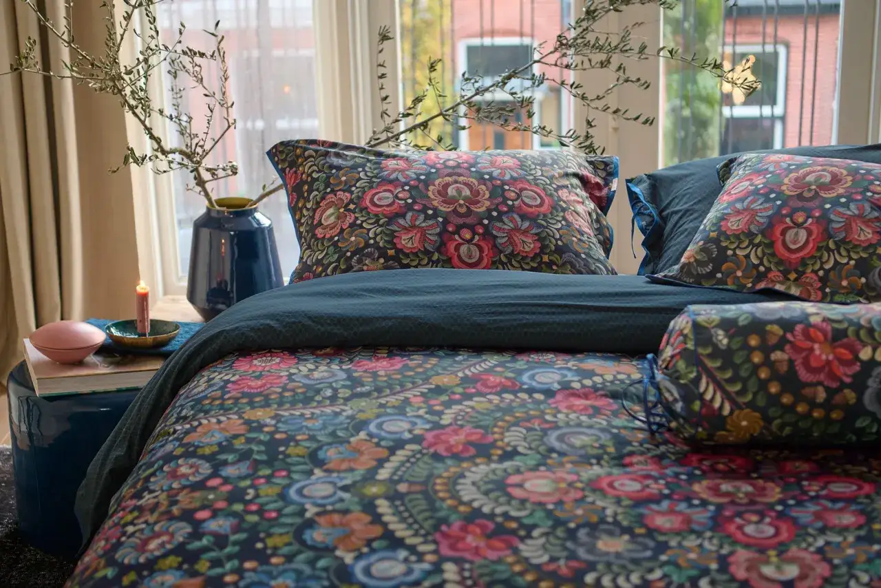 Ein Bett mit floral gemustertem Perkal-Bettzeug, das an einen &uuml;ppigen Garten erinnert. Kissen und Decken zeigen bunte Blumenmuster.