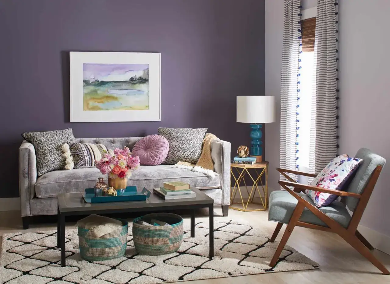 Ein gemütliches Wohnzimmer mit lila Wänden. Welche Farbe passt gut zu lila? Hier: Türkis, Rosa und Goldtöne harmonieren perfekt.