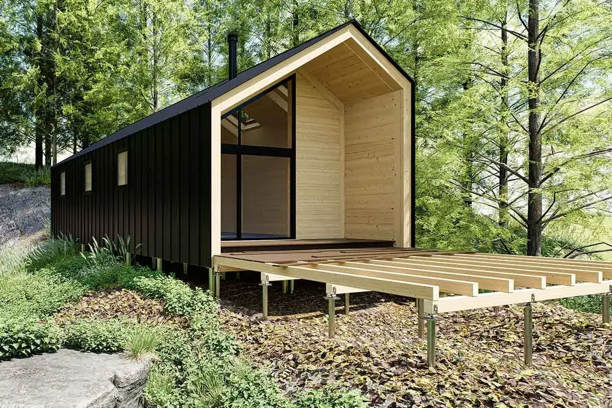 Modernes Holzhaus im Wald, dessen Terrasse renovieren wird. Die Holzkonstruktion steht auf Stelzen, umgeben von üppiger Vegetation.