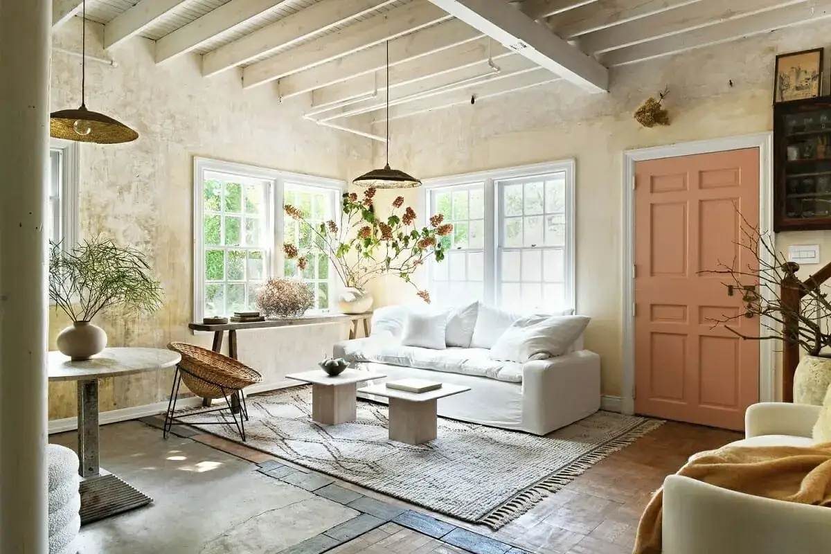 Gem&uuml;tliches Wohnzimmer mit wei&szlig;em Sofa, Korbstuhl und rustikalen Akzenten, die auf nachhaltige Materialien wie Holz und Naturfasern hinweisen.
