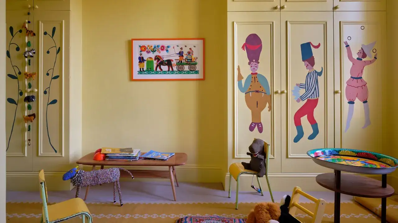 Ein fr&ouml;hliches Kinderzimmer mit gelben W&auml;nden und Schr&auml;nken, die mit bunten Motiven bemalt sind. Ein Bild mit einer Pferdekutsche und Spielzeugtiere schm&uuml;cken den Raum.