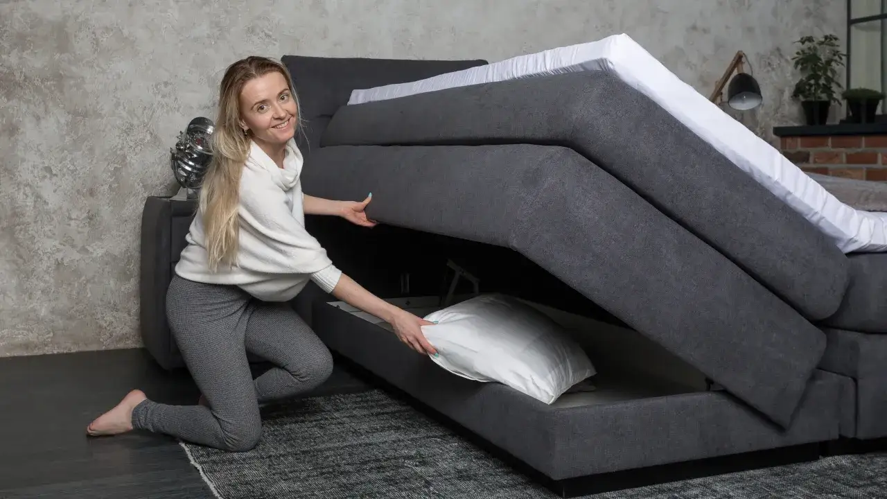 Frau verstaut Kissen in einem Boxspringbett mit Stauraum. So beziehe ich ein Boxspringbett &ndash; mit praktischem Platzangebot.