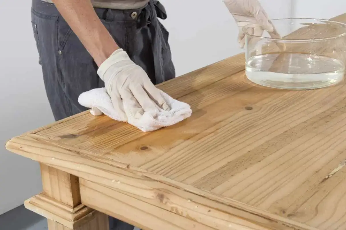 Person mit Handschuhen wischt mit einem Tuch über einen Holztisch, um ihn für das tisch lackieren vorzubereiten.
