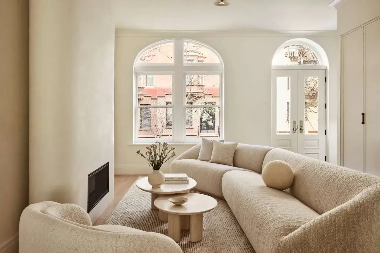 Ein gem&uuml;tliches Wohnzimmer mit geschwungener Couch, zwei runden Couchtischen und einem Kamin. Helle Wandfarben schaffen eine warme Atmosph&auml;re.