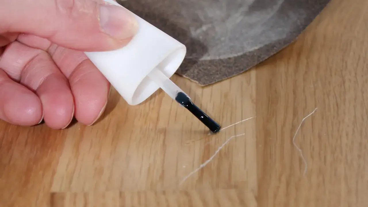 Mit einem Lackstift werden Kratzer auf dem Parkett ausgebessert. Schleifpapier liegt bereit.