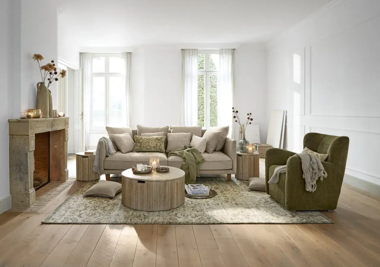 Gem&uuml;tliches Wohnzimmer mit beigem Sofa, Kamin und gr&uuml;nen Akzenten. Die Farbe beige dominiert den Raum und schafft eine warme Atmosph&auml;re.