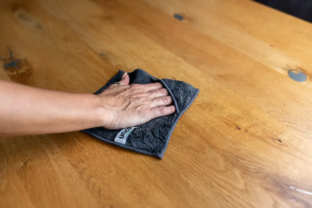 Hand wischt mit Tuch über Holzoberfläche, um schwarze Flecken zu entfernen. Hausmittel-Tipp für sauberes Holz.