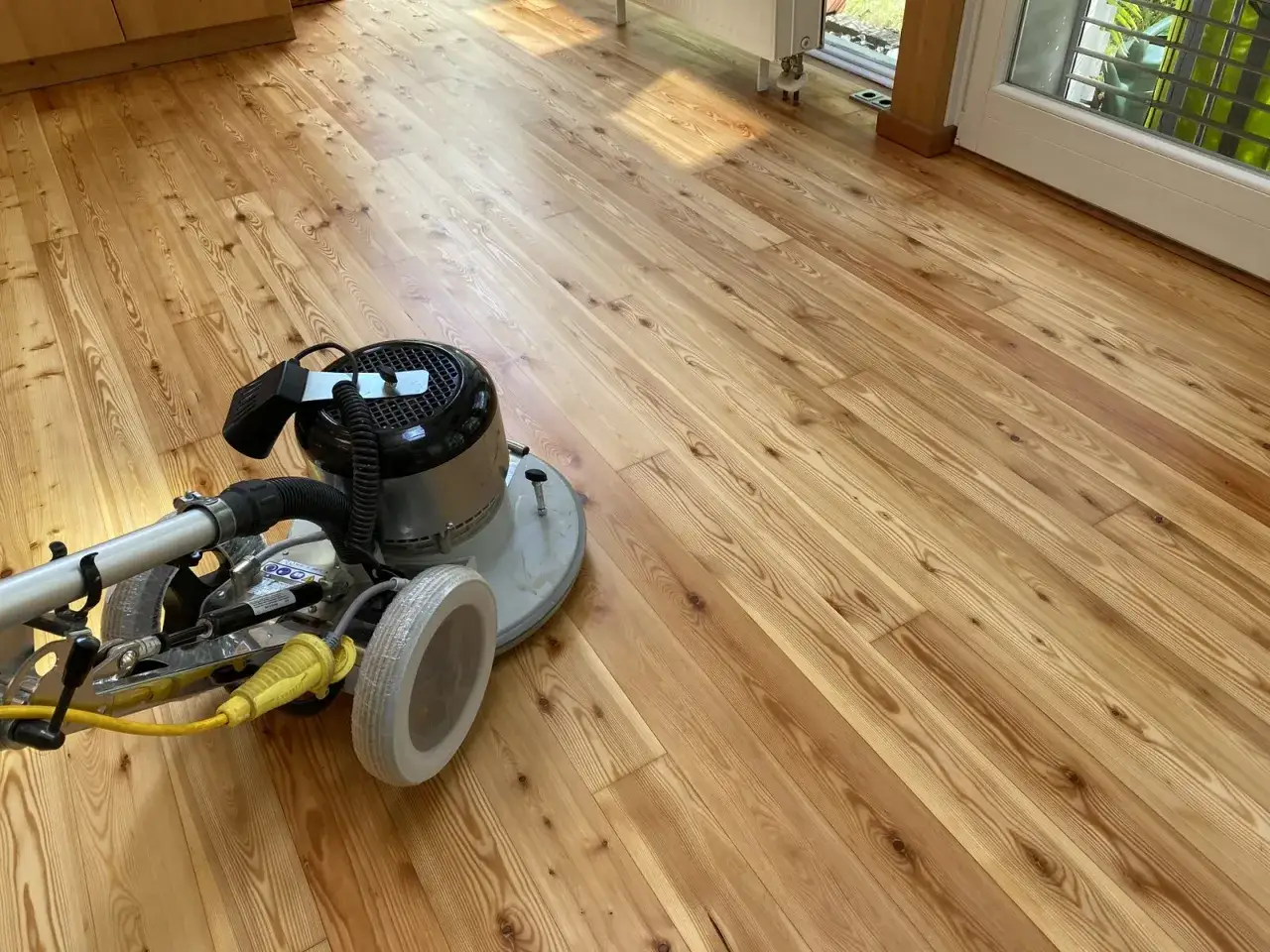Maschine zum Parkett versiegeln steht auf hellem Holzboden. Sonnenlicht fällt auf die Dielen.