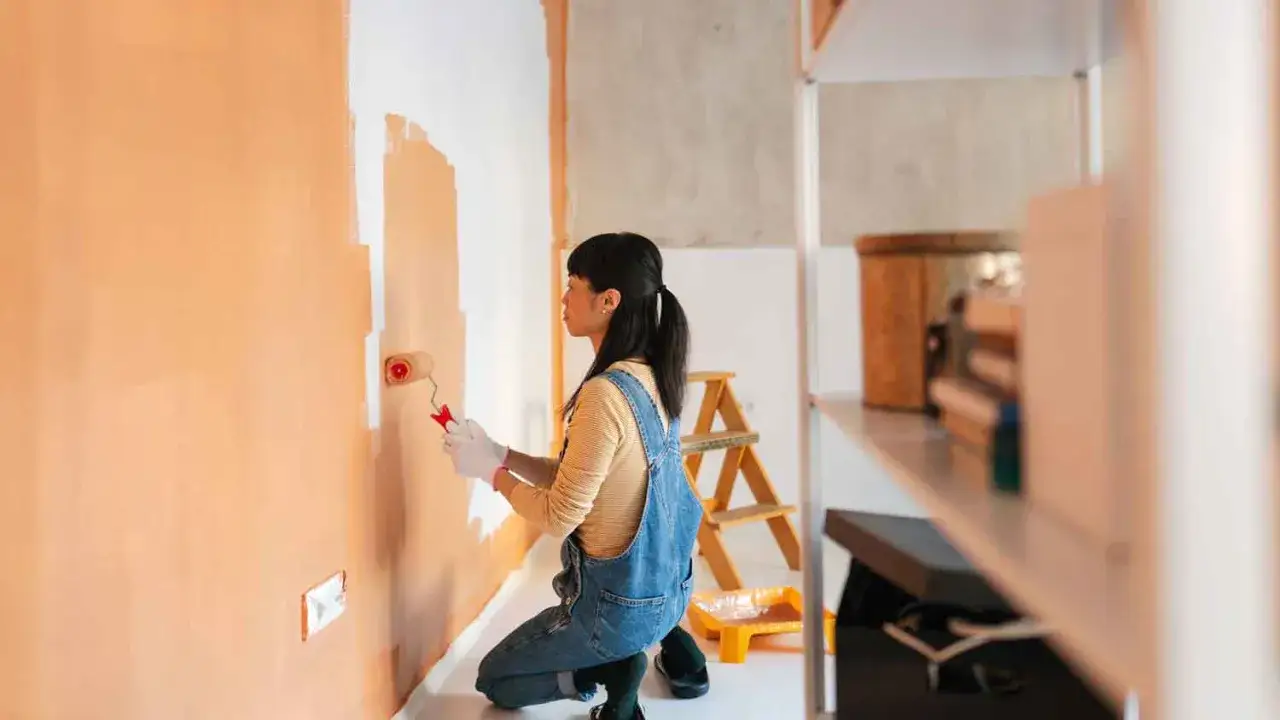 Frau malt Wand in Orange. Sie fragt sich, wie lange braucht wandfarbe zum trocknen, während sie die Farbe aufträgt.