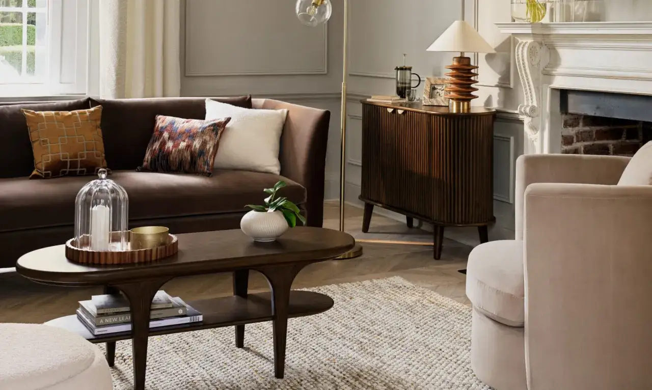 Gem&uuml;tliches Wohnzimmer mit braunem Sofa und Kissen, die blau und braun kombinieren. Ein Holztisch und ein Teppich runden das Bild ab.