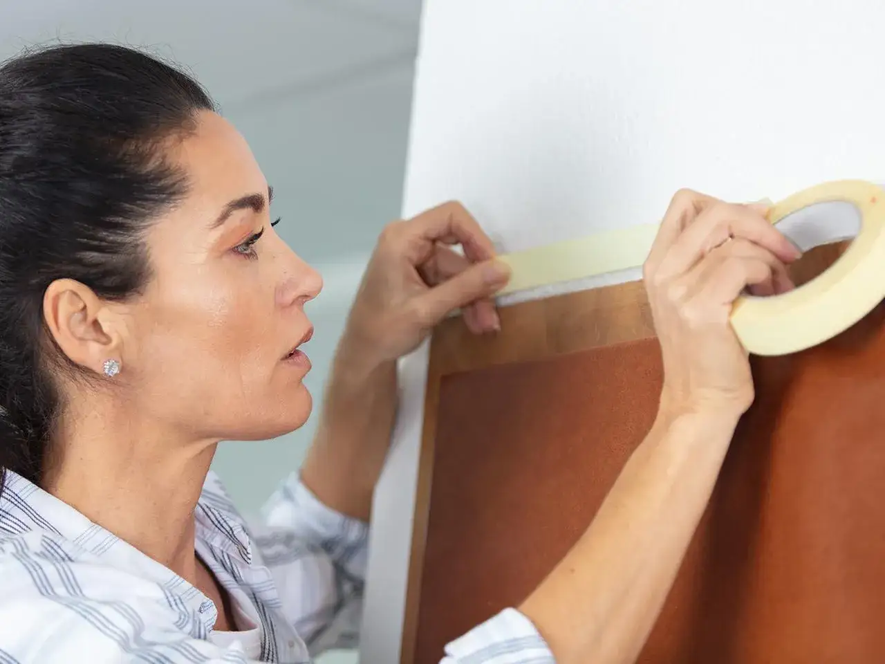 Frau klebt sorgfältig die Wand ab, um eine gerade Kante für Malerarbeiten zu schaffen.
