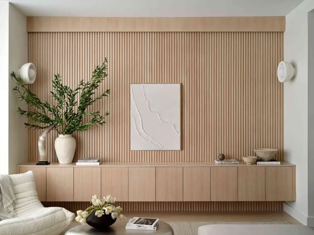 Ein Wohnzimmer mit vertikalen Holzpaneelen in neutralen Farben. Ein Kunstwerk mit Textur h&auml;ngt an der Wand.