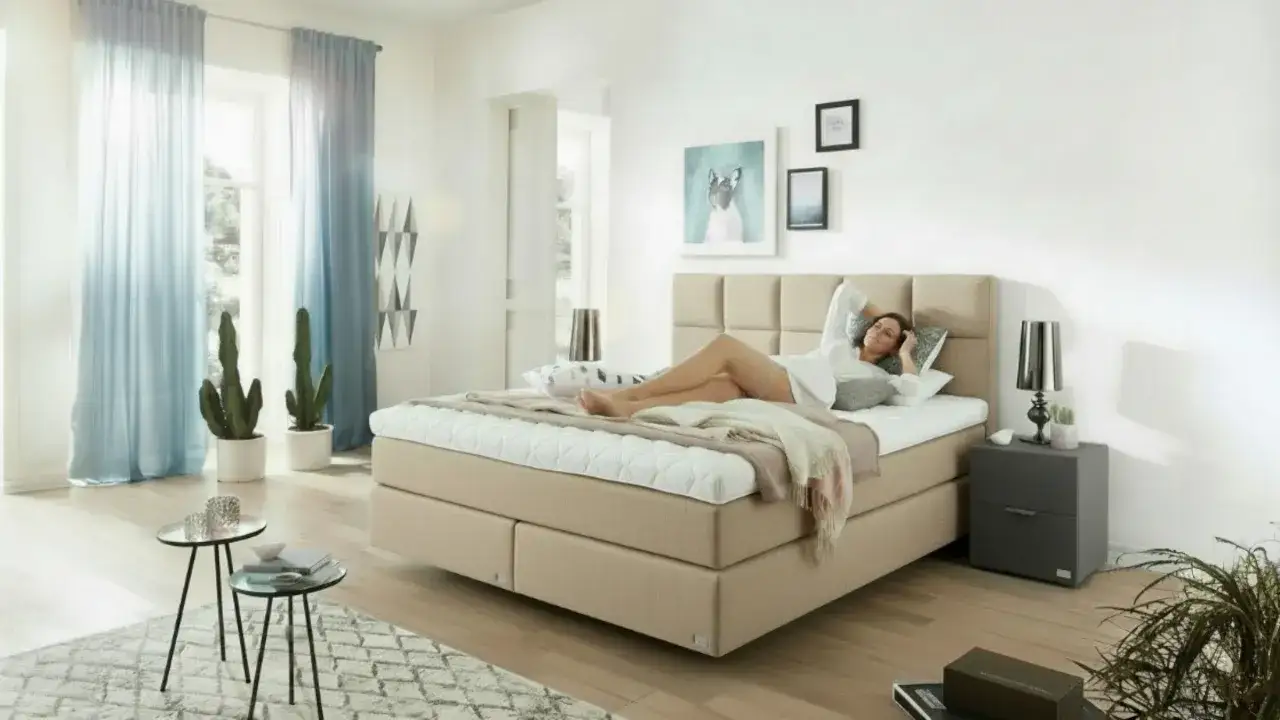 Frau liegt entspannt auf einem Boxspringbett, das ihr zu hart ist. Sie genießt den Komfort, obwohl sie sich mehr Weichheit wünscht.