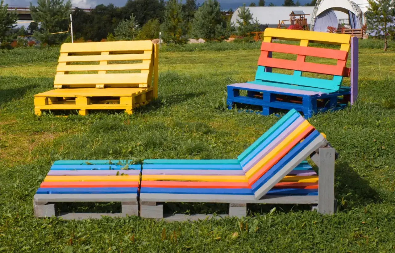 Bunte Palettenm&ouml;bel im Garten: Eine Liege und zwei B&auml;nke, farbenfroh gestaltet. Paletten streichen ohne schleifen ist hier die Devise f&uuml;r kreative Deko.
