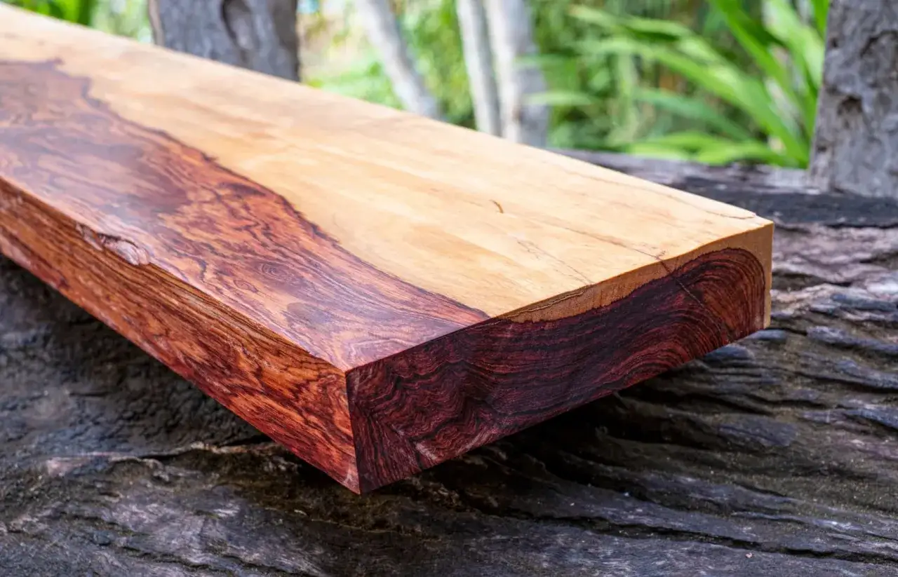 Ein Brett aus dem teuersten Holz der Welt, mit tiefroten und hellen Maserungen, liegt auf grobem Holz.