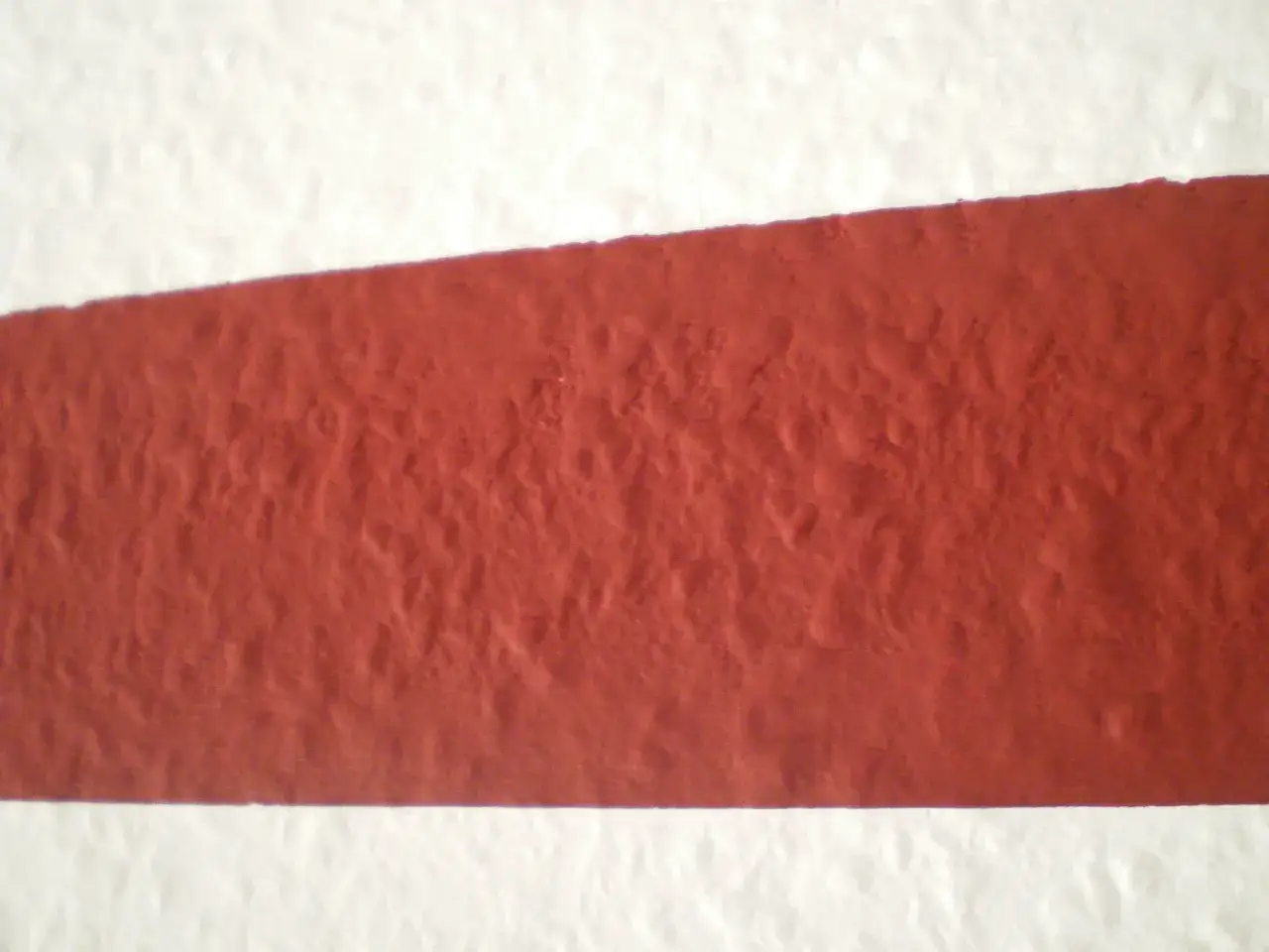 Eine rote Fl&auml;che, die wie ein Streifen aussieht, wird auf eine wei&szlig;e Wand gemalt.