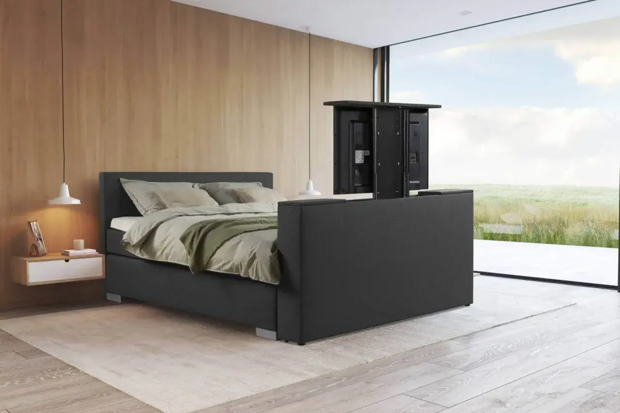 Modernes Schlafzimmer mit einem Bett, das einen versteckten Fernseher am Bettende integriert. Gemütliche Atmosphäre mit Holzwand und großem Fenster.