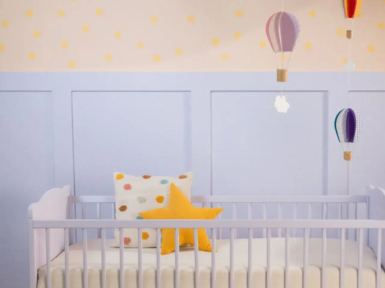 Ein frisch gestrichenes Kinderbett in zartem Lila, dekoriert mit einem Sternkissen und bunten Heißluftballons.