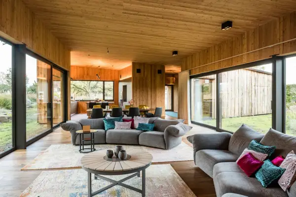 Gemütliches Wohnzimmer mit holzverkleideten Wänden und Decke, das zeigt, wie man eine holzdecke modern gestalten kann. Große Fensterfronten bieten Blick ins Grüne.