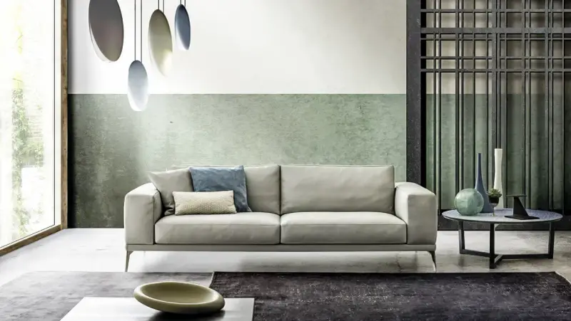 Modernes Wohnzimmer mit hellem Sofa, grüner Wand und stilvollem farbkonzept. Hängende Lampen und dekorative Vasen ergänzen das Ambiente.